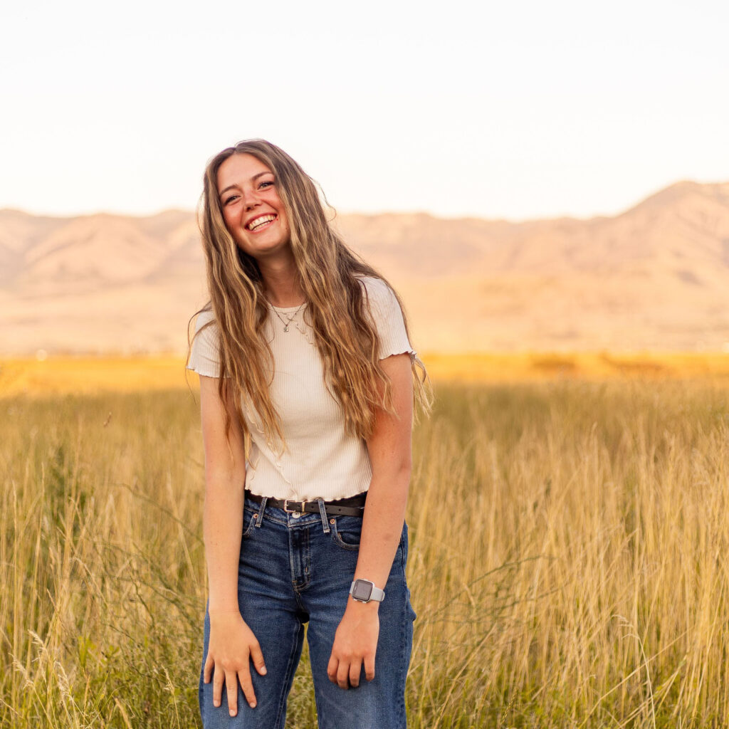 Anna standing in wheat field with mountains and sky in the background.